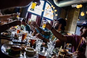 A City Brew Tours group raising beer glasses in a cheers while sitting at a meal and beer pairing.