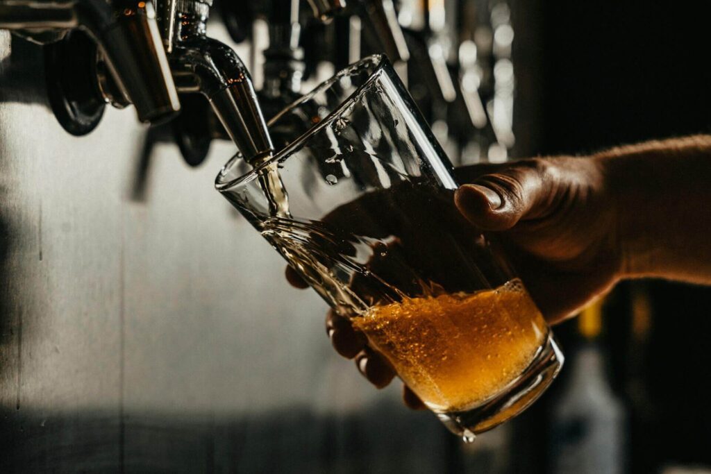 Barman pouring a beer into a transparent tall glass