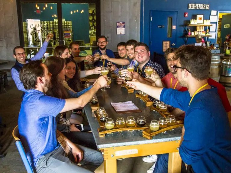Group of friends enjoying a craft beer tasting during a food and drink tour in Montreal, cheerful toast around a table with beer samples