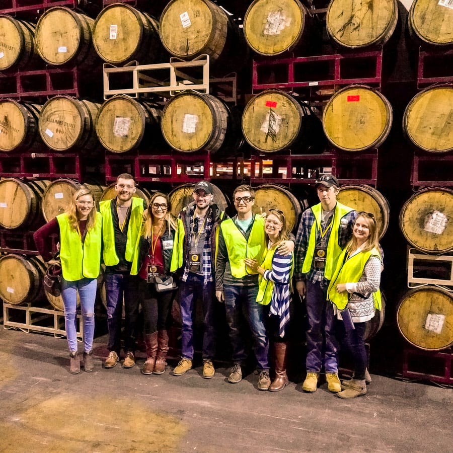 A private tour poses in front of a wall of beer barrels