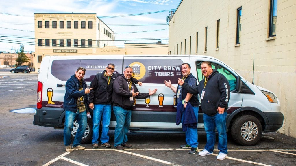 A group of guests stand in front of the City Brew Tours bus