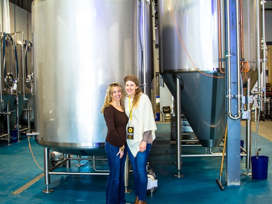 Two City Brew Tours guests pose in front of Goodwater's steel tanks